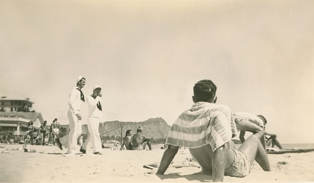 Two sailors walk in uniform on beach. Diamondhead in background, 1940s