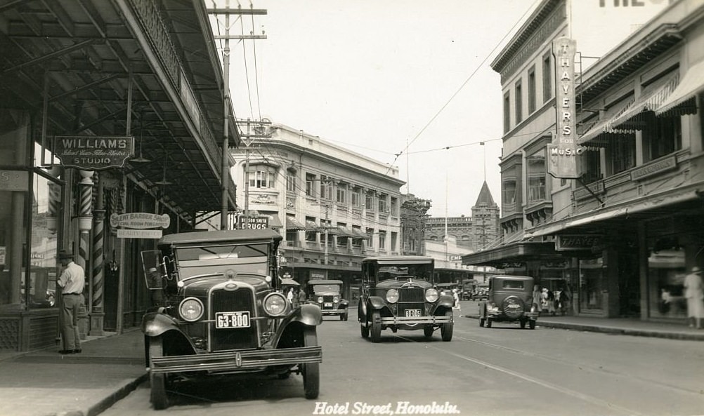 City street scene with cars, barber poles and a few pedestrians, 1940s