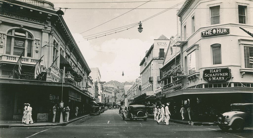 Broad commercial street with cars and sailors, 1940s