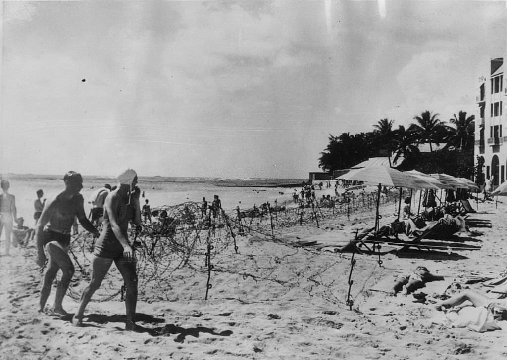 The beach of the Royal Hawaiian Hotel in Honolulu which has been leased by the American navy for officers and men on leave. The barbed wire on the beach does not stop them enjoying a swim, 1940s