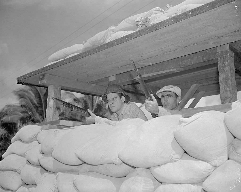These two men, behind makeshift sand barricades, are two company employees, who take time out from their regular work, to stand guard with rifles cocked, against any possible Japanese move.