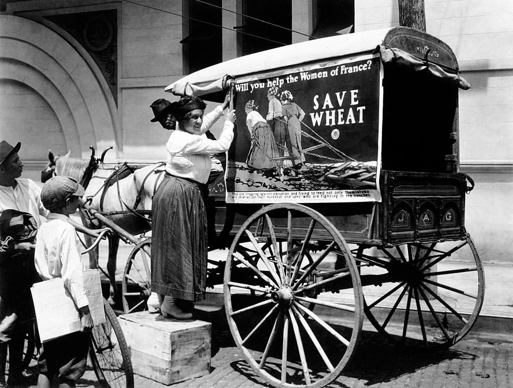 Tacking up a United States Food Administration poster encouraging people to "Save Wheat" and help the women of France during World War One in Mobile, Alabama, 1918.