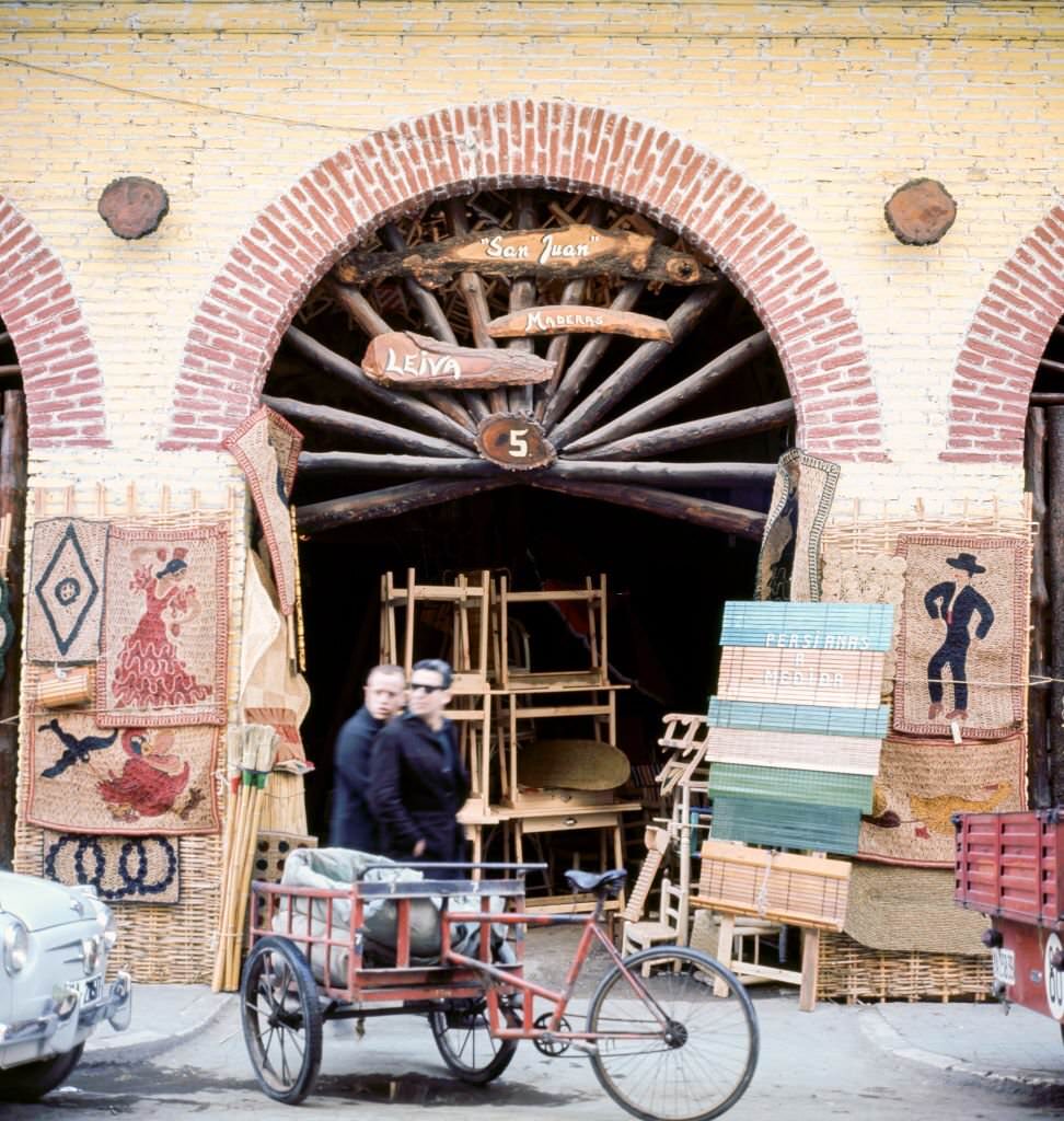 View of pedestrians as they walk past an antiques shop, Malaga, Andalusia, Spain, 1964.