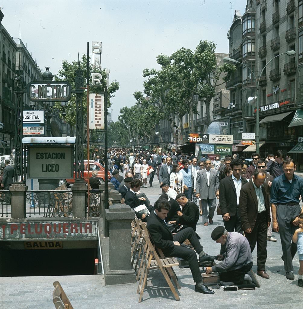 Shoe shiners work alongside the bustling tree-lined walkway of Ramblas de San Jose, Barcelona, Spain.