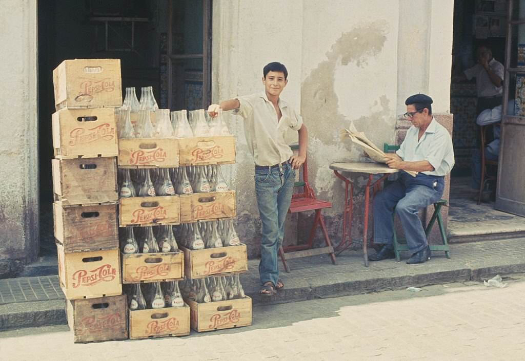A man standing next to crates containing empty Pepsi bottles in El Puerto de Santa María, Cádiz, Spain, 1960.