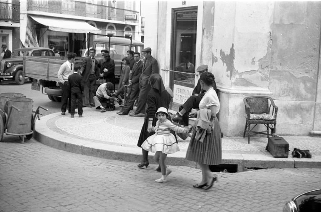Street scene People in front of a shop entrance. A little girl, wears a skirt and a hat, is hold by two women