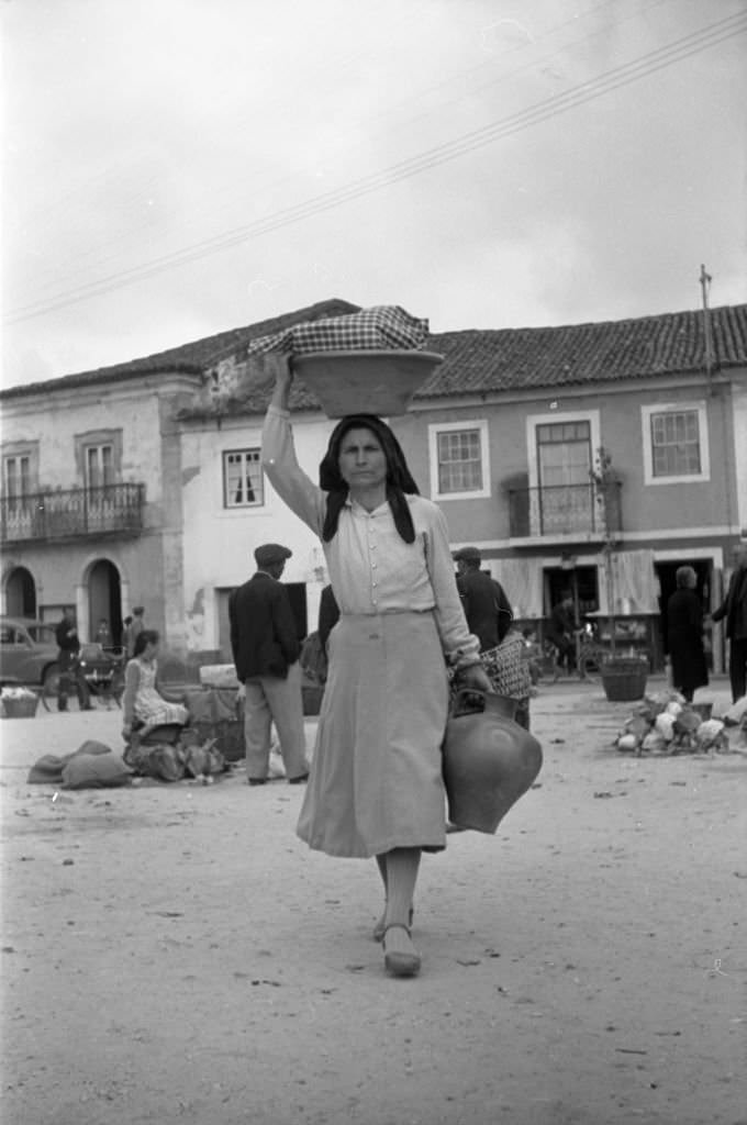 A woman carries a basket on her head and a big ewer in her hand, 1960
