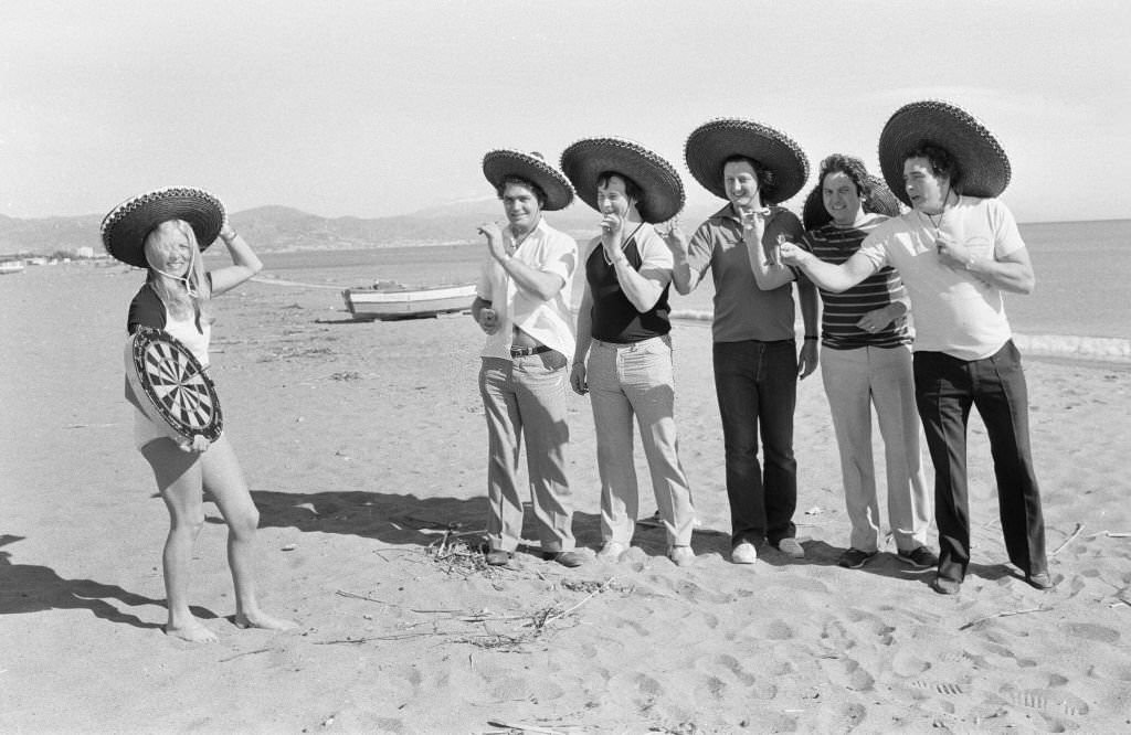 British darts player Eric Bristow poses on the beach with Maureen Flowers and fellow British drafts players at Torremolinos Del Mar on the Costa Del Sol in Spain ahead of the Mediterranean Open Darts Championship, 31st January 1982.