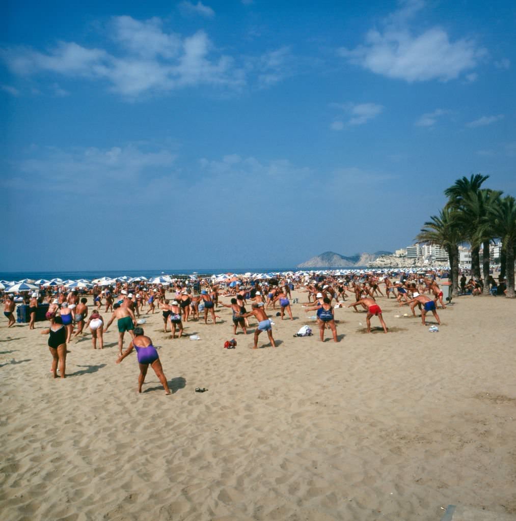 Tourists doing their early morning exercises at the beach of Benidorm, Spain 1980s.