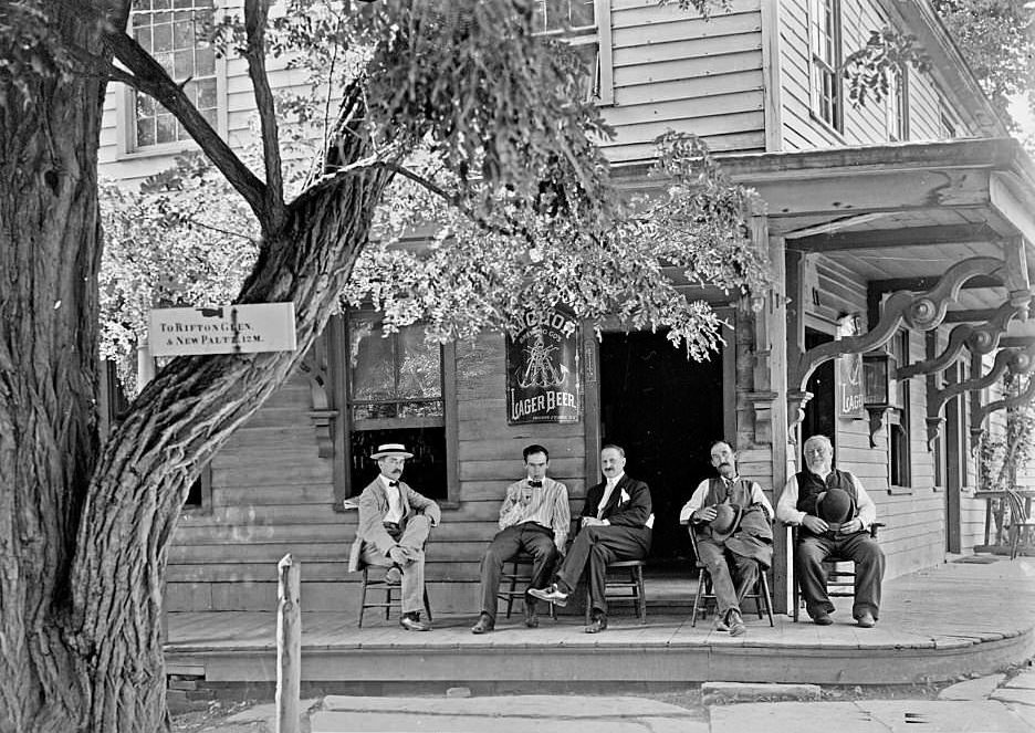 Five men sitting on the porch of a building that has Anchor Lager Beer signs next to its entrances, 1904.