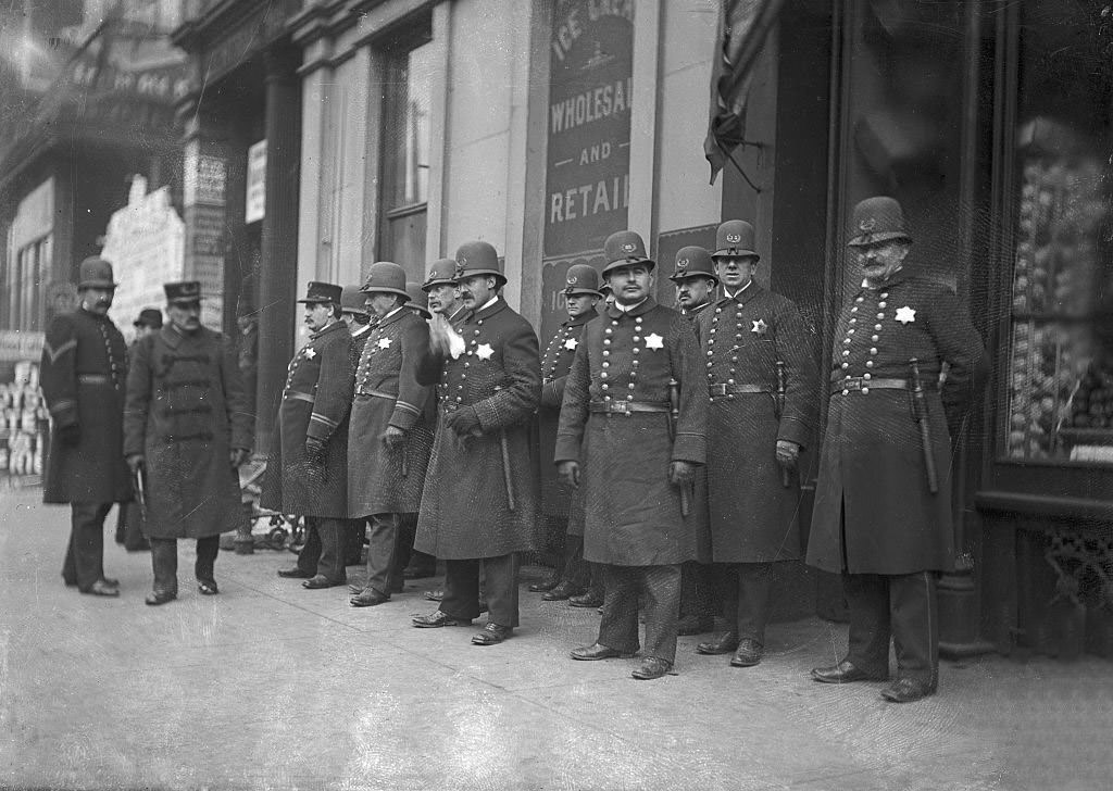 A police officer walking in front of a group of policemen gathered along a sidewalk in front of a store during the Chicago City Railway Strike, Chicago, Illinois, 1903