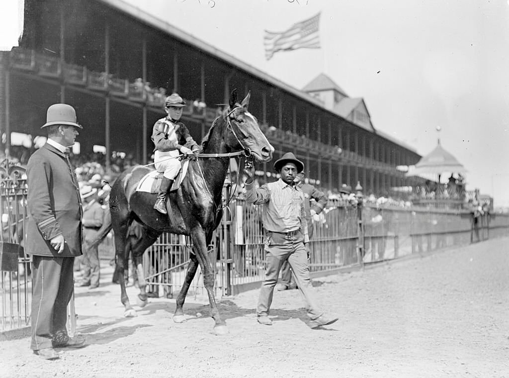 Racehorse, Lute, with jockey mounted, being led on track by African American handler, Washington Park Race Track, Chicago, 1903.