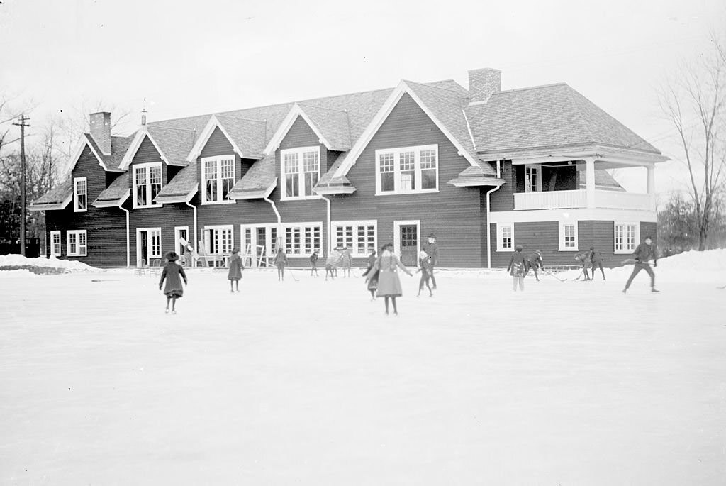 Exterior view of Humboldt Park Boathouse with children ice skating and playing hockey on the frozen lagoon nearby in Humboldt Park in the Humboldt Park community area of Chicago, Illinois, 1903.