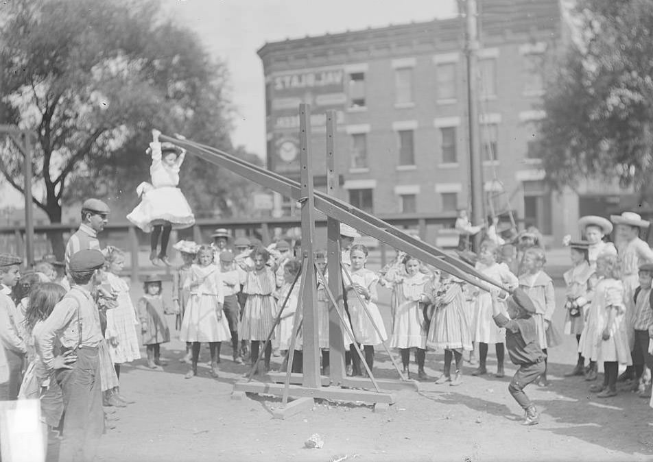 Children playing on a seesaw at the Webster School playground, located at Wentworth Avenue and 33rd Street in the Douglas neighborhood, Chicago, Illinois, August 19, 1902.