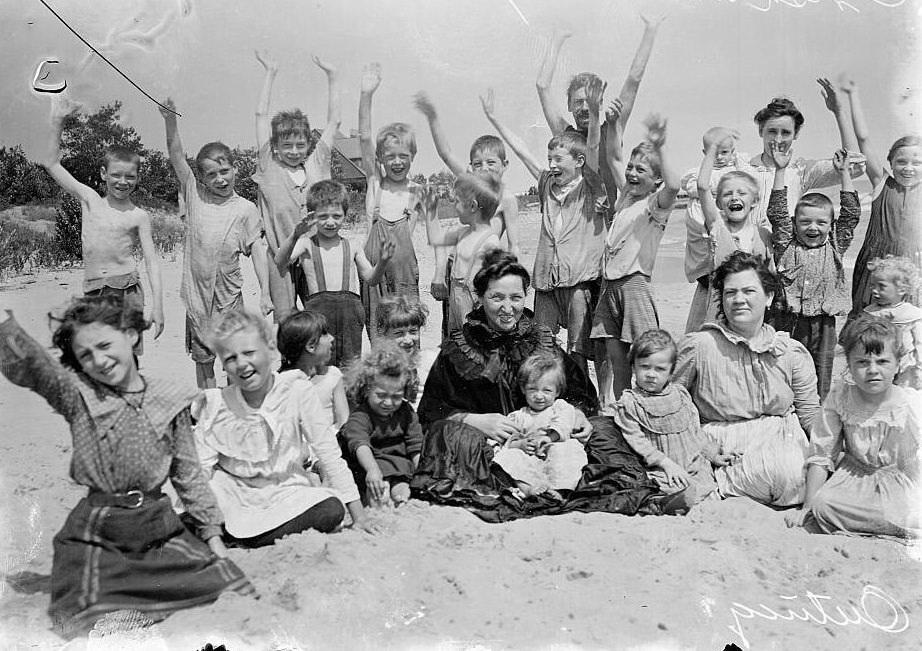 Women and children sitting on a sandy beach while on a Chicago Daily News Fresh-air outing in Chicago, Illinois, 1902.
