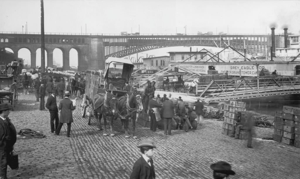 A men unloading crates and barrels from horse-drawn wagons by the waterfront at the docks of Chicago, Illinois, 1905