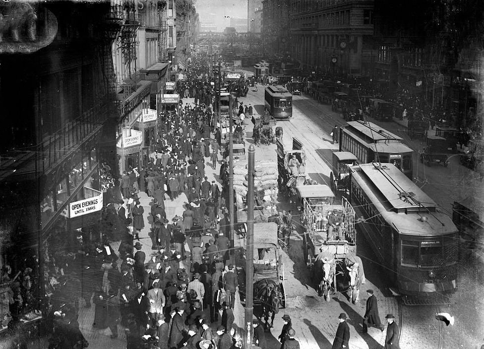 Shoppers on State Street, with a streetcar approaching curved track and a two-horse team pulling a wagon in the foreground, Chicago, Illinois, 1900s.