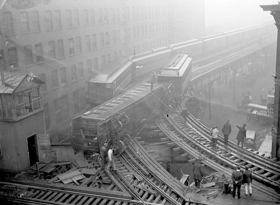 Elevated train wreck, with one train car off its tracks and lying across the adjacent track in front of another elevated train, 1900s.