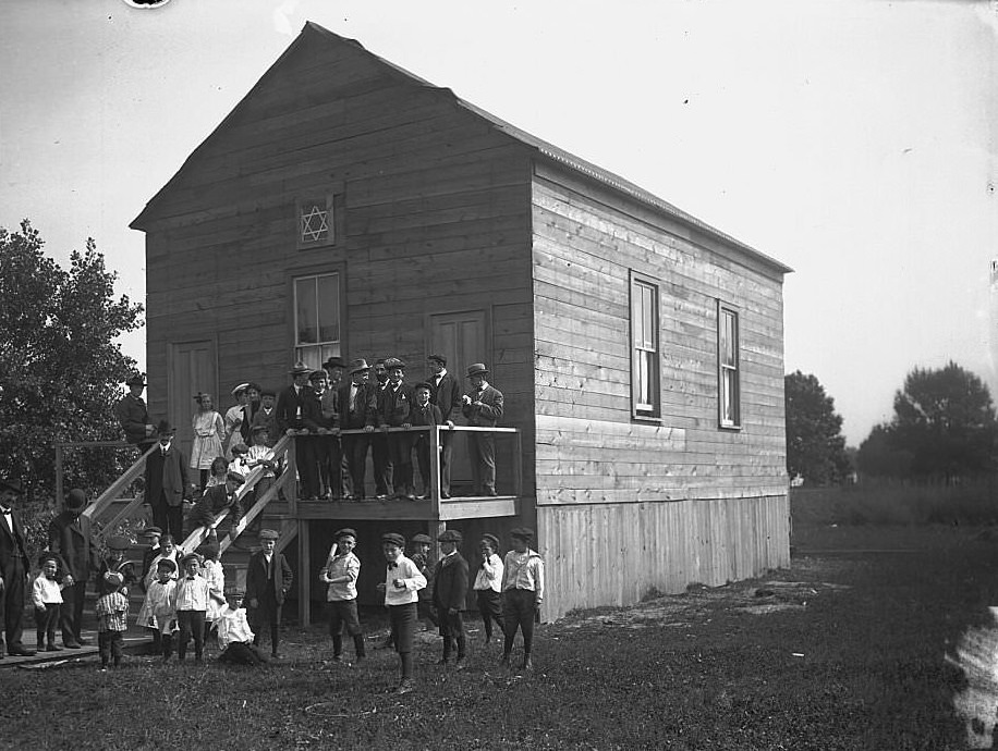 Exterior view of a synagogue with a group of children and men standing on its porch and on the ground in front, Maywood, Illinois, 1905.