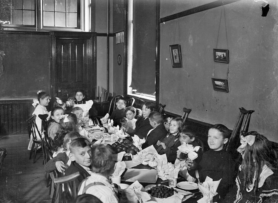 Children with handicaps sitting around a table with food in a classroom, Chicago, Illinois, 1905.