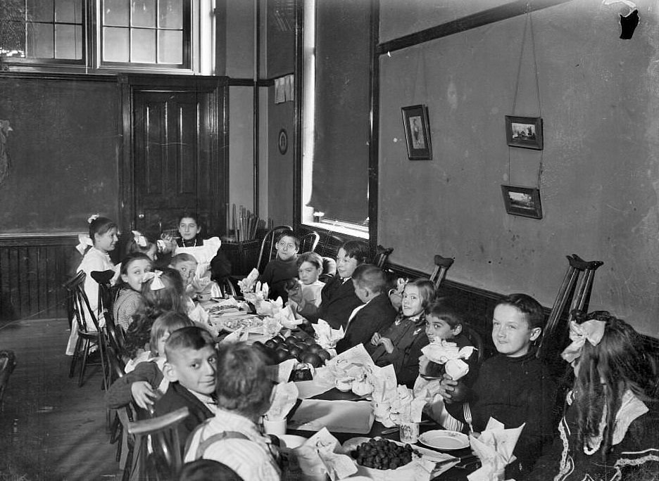 Children with handicaps sitting around a table with food in a classroom, Chicago, Illinois, 1905.