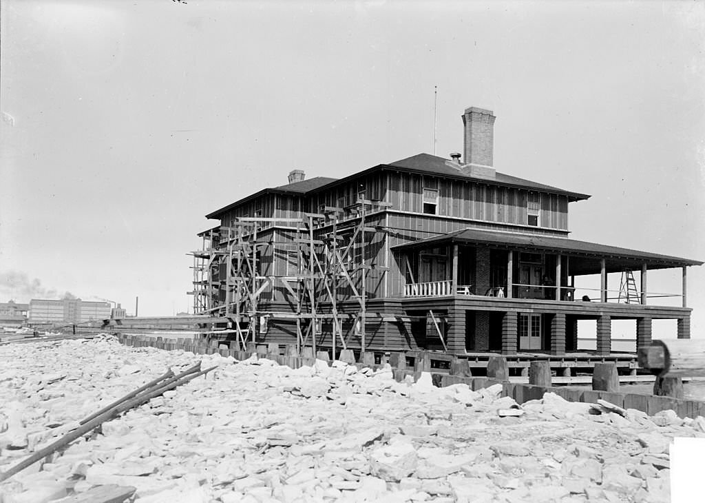 Exterior view of a Chicago Yacht Club boathouse under construction with one side covered in scaffolding and the porch partially finished, 1901.