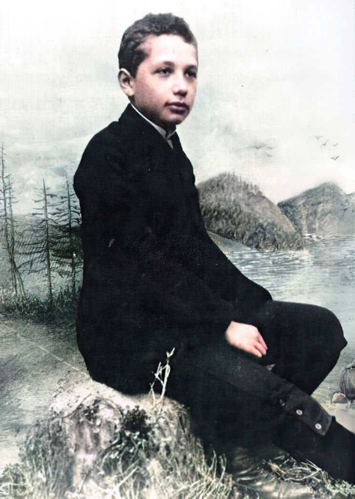 Albert Einstein when he was fourteen years old, wearing a black suit and a calm expression and posing in front of an outdoor backdrop, 1893.
