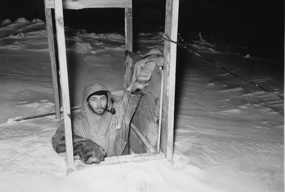 Dr. Wade, crew member, leaving the Snow Cruiser through a hatch in the surrounding snow.
