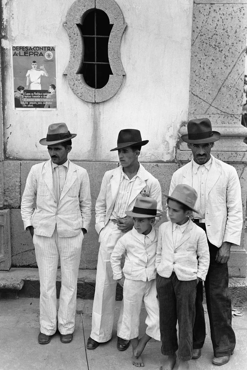 Men and boys at the church of Bom Jesus de Matosinhos stand in front of an anti-leprosy campaign poster.