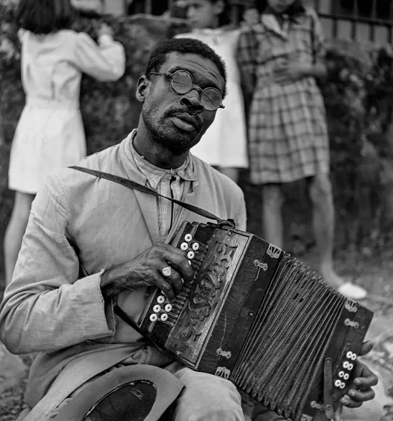 A blind street performer plays the accordion.