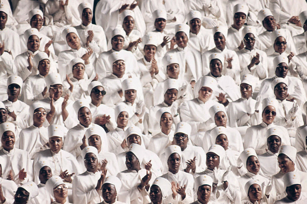 Muslim women dressed in white applaud Elijah Muhammad during the delivery of his Savior’s Day Message in Chicago, March 1974.