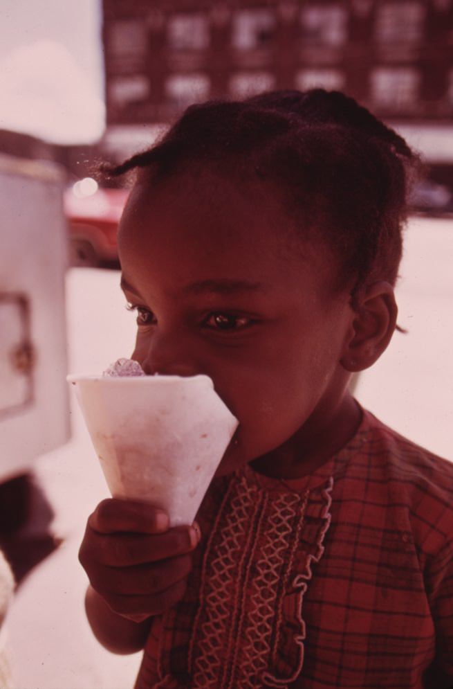 A child savors a snow cone just received from a sidewalk vendor on Chicago’s West Side.