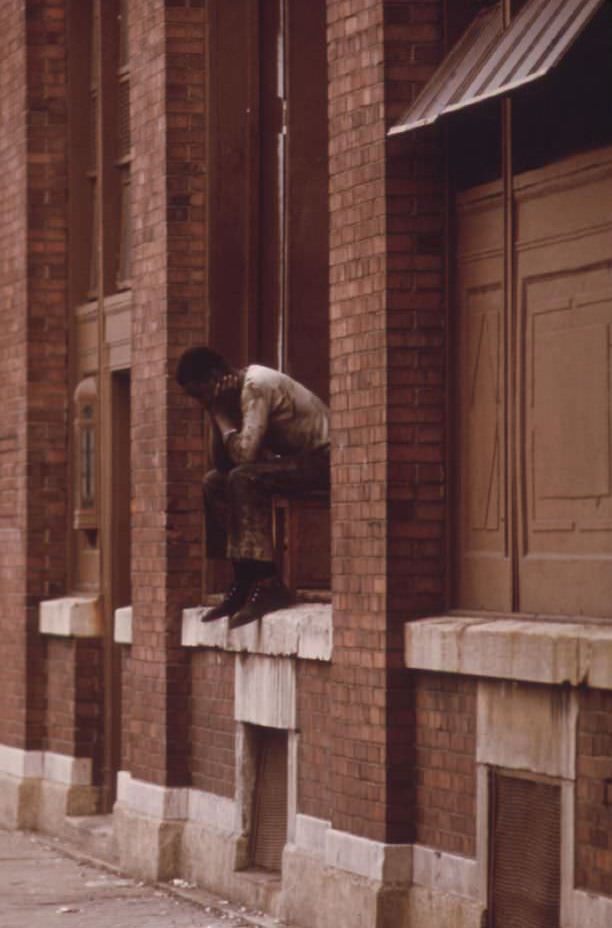 A black man who is jobless sits on the windowsill of a building in a high crime area on Chicago’s South Side, he has nothing to do and nowhere to go.