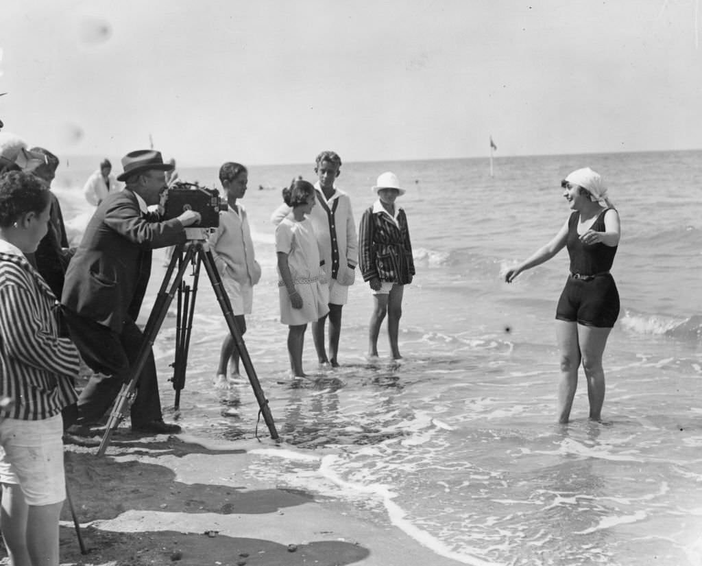 A woman being filmed by cine camera as she paddlles in the sea on a beach at Deauville, 1922