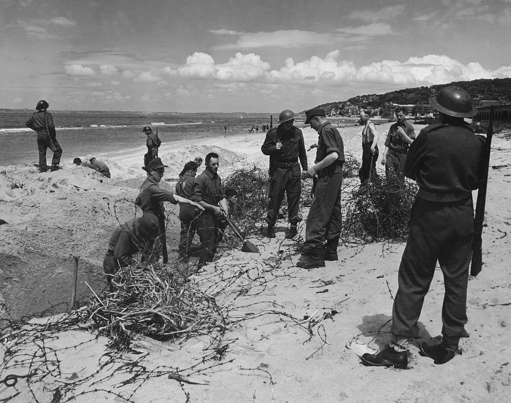 These German prisoners of war are cleaning some of the barbed wire and steel obstructions at the beach resort of Deauville