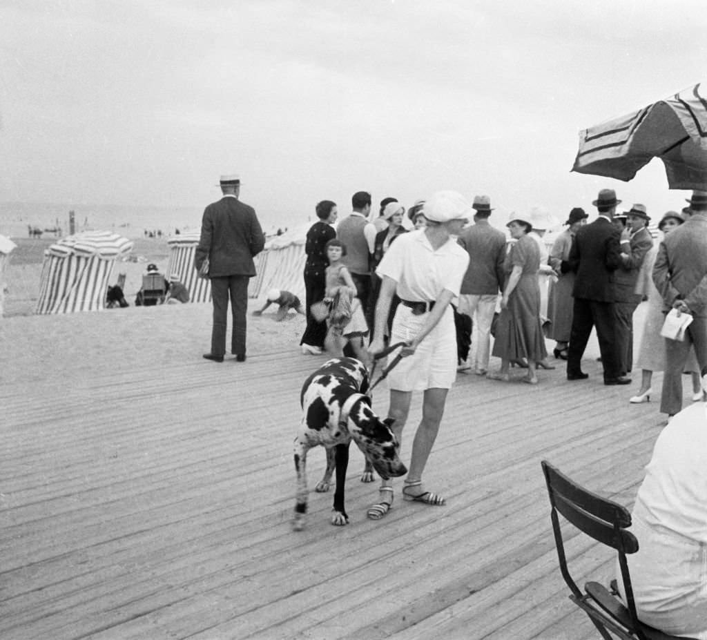 Woman holding her dog on a leash on the planks by the beach, in Deauville, France in 1938.