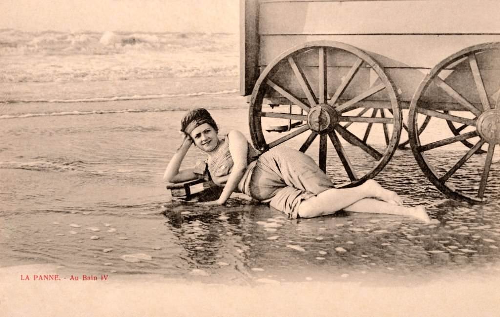 A young woman wearing a swimming costume posing beside a bathing hut in the sea, 1910.