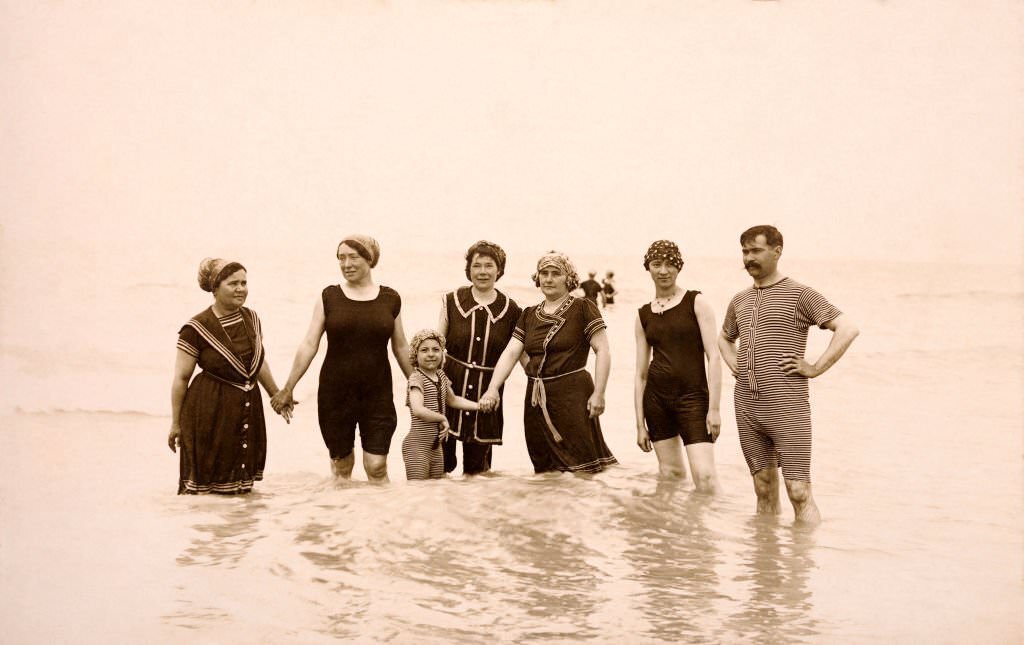 A small group of people wearing swimming costumes paddling at Deauville, 1910