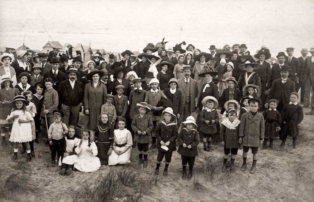 A large group of people in their Sunday best on a holiday outing at a beach with beach huts at Deauville, 1910