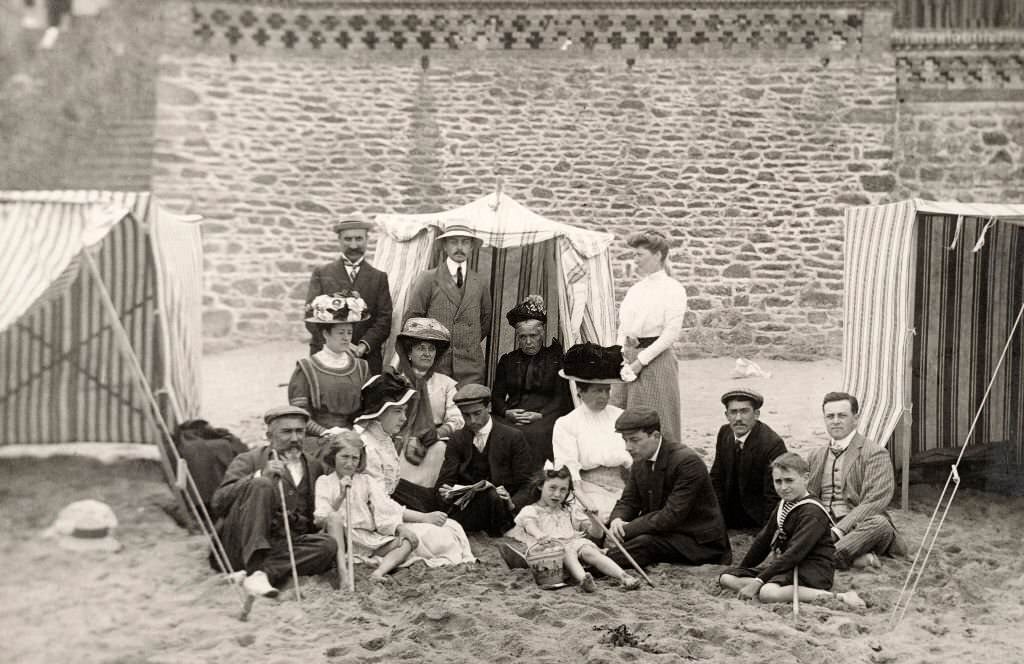 A family group wearing their Sunday best sitting on the sand at a beach at Deauville, 1910