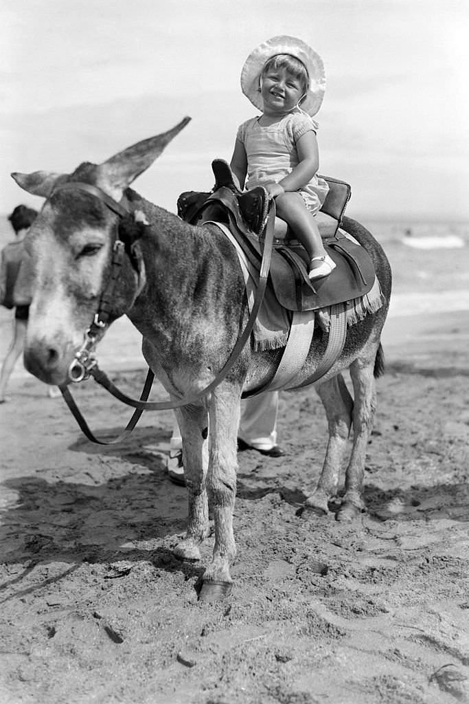 Jackie Garai, daughter of Alexandre Garai, founder of Keystone press agency, enjoying a donkey ride on a beach in August 1932 in Deauville