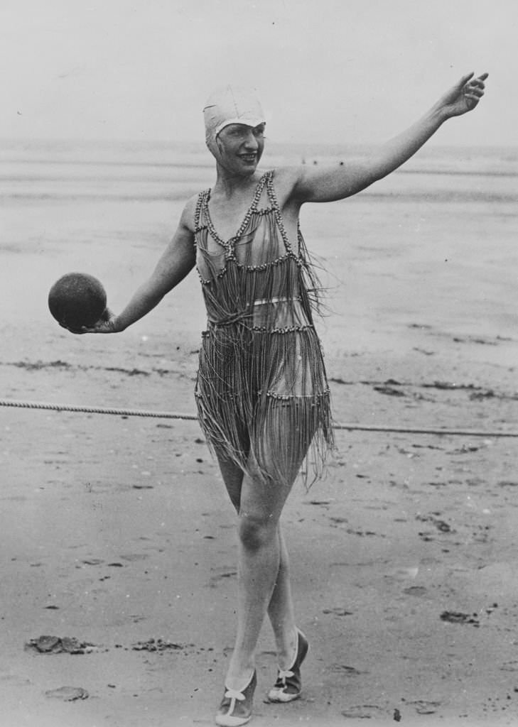 A woman wearing a bathing cap and suit plays with a ball on Deauville Beach.