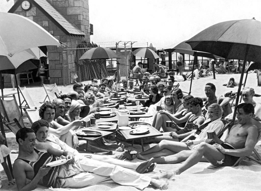 Members of the Deauville Club have their weekly breakfast meetings on the beach after a quick dip in the surf, 1930