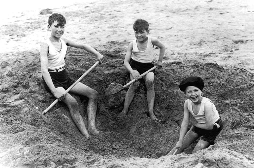 In August 1929, on Deauville beach, these three children dug a hole in the sand with shovels.