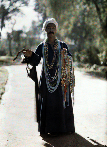 Souvenir merchant walks carrying beads and necklaces.