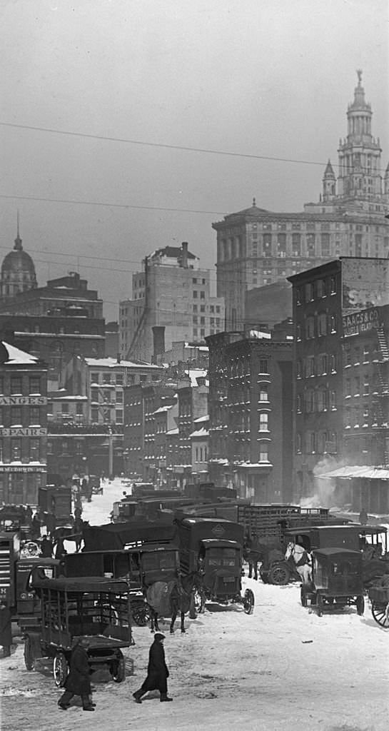 A view of a group of automobiles and wagons parked in the snow at the Fulton Street Fish Market, in downtown Manhattan, New York City. 1920s