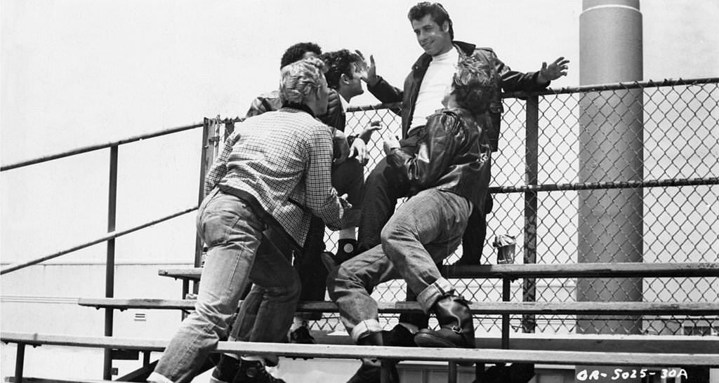 John Travolta with his crew on the bleachers in the 'Summer Nights' scene from the Paramount musical, 'Grease', 1978.
