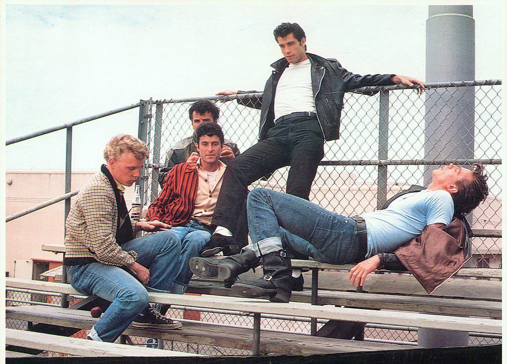 John Travolta hanging out with his crew on the bleachers in a scene from the film 'Grease', 1978.