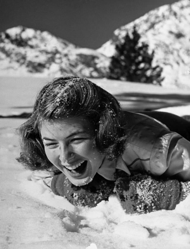 Ingrid Bergman screaming with laughter as she lies splashed with snow by a playmate during her ski vacation at June Lake resort, 1941.