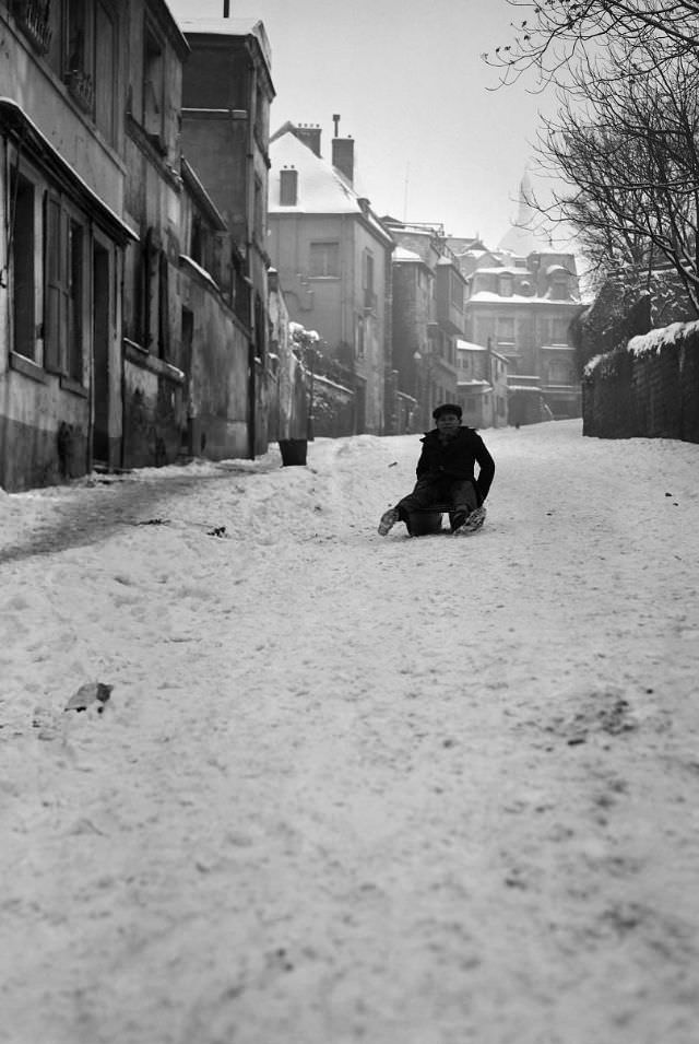 A boy sleds in the snow-covered rue de l'Abreuvoir in Montmartre, Paris, France, January 1945.
